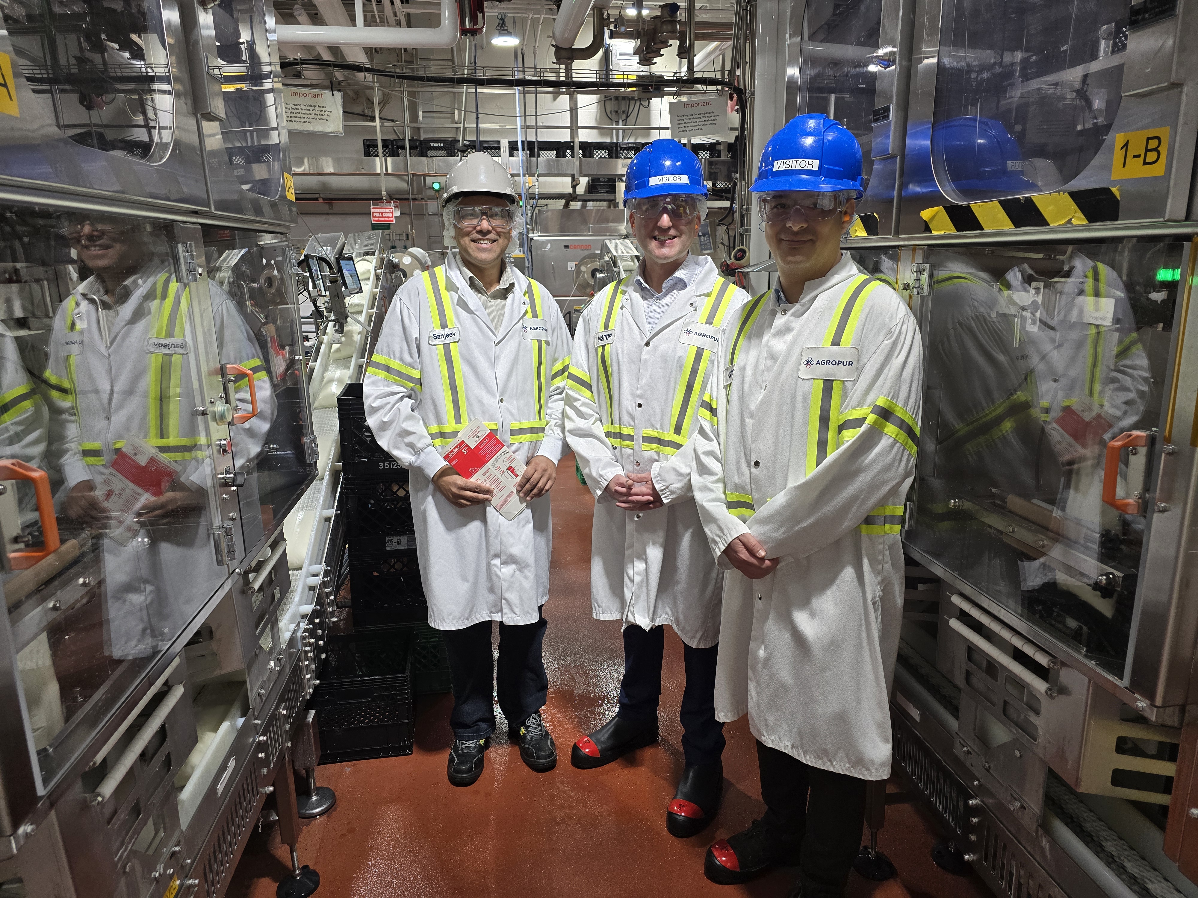 Three men standing inside a dairy plant in lab coats and protective gear